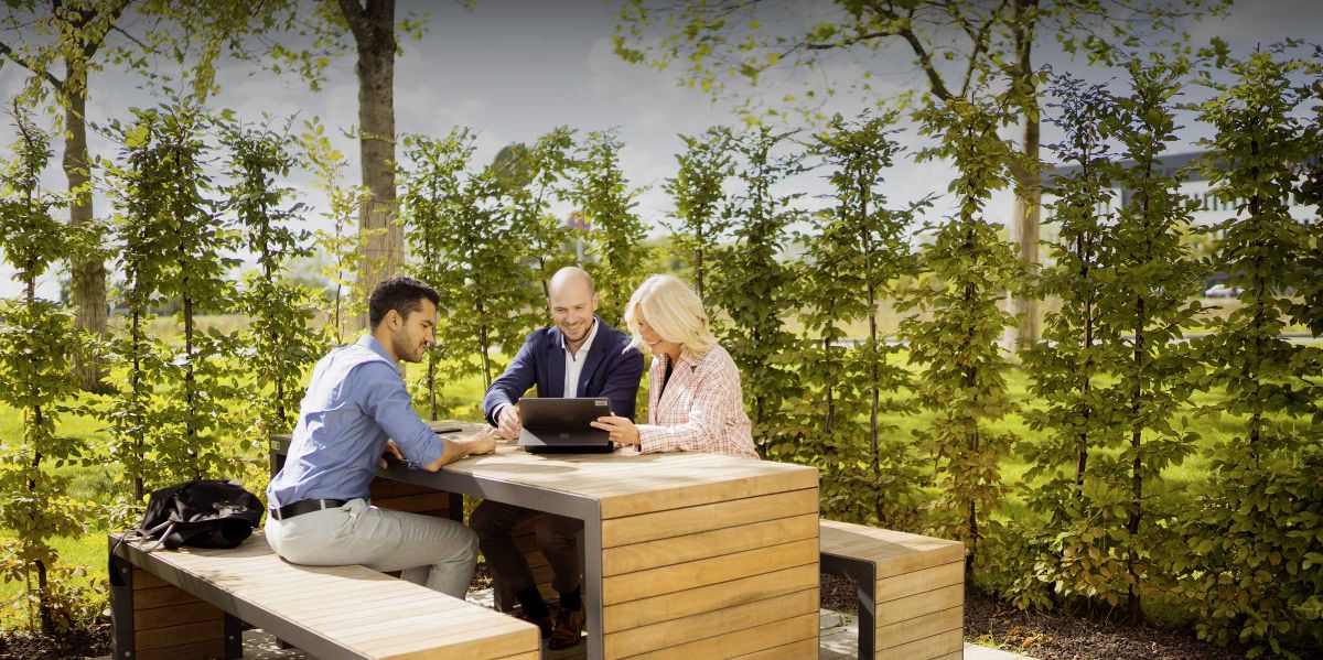 Mitarbeiter arbeiten gemeinsam mit dem Laptop auf einer Bank im Grünen am Business Campus Unterschleißheim