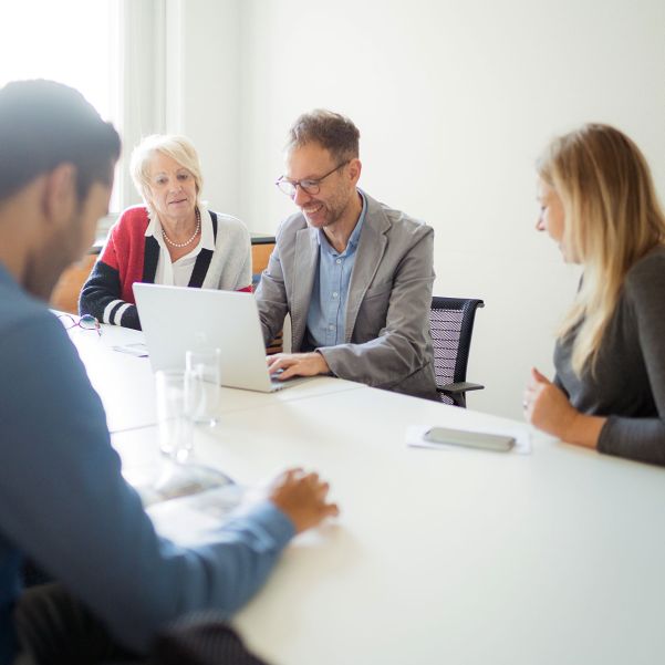 Several colleagues sit in a meeting in a pleasant atmosphere and look at a laptop together