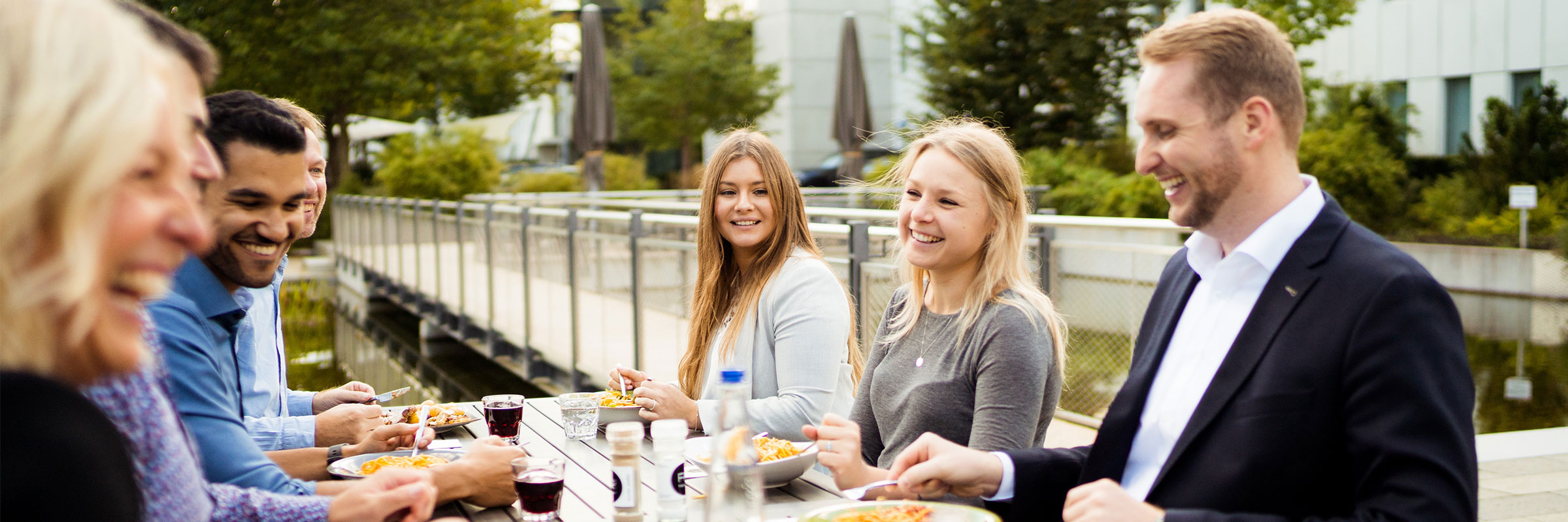 Mitarbeiter sitzen gemeinsam auf der Terrasse und genießen das frische und abwechslungsreiche Mittagsangebot am Business Campus Unterschleißheim
